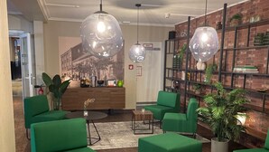 A modern lounge area with green upholstered seating, a wooden coffee table, and a brick wall with a mural. - Hotel Dampfmühle (Neukirchen-Vluyn)