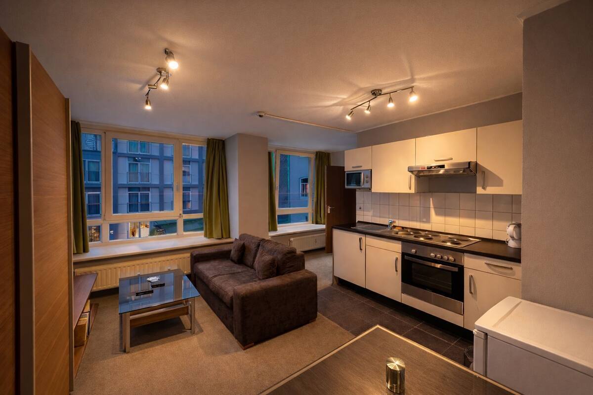 A compact living space with a kitchenette, a sofa, a coffee table, and large windows.