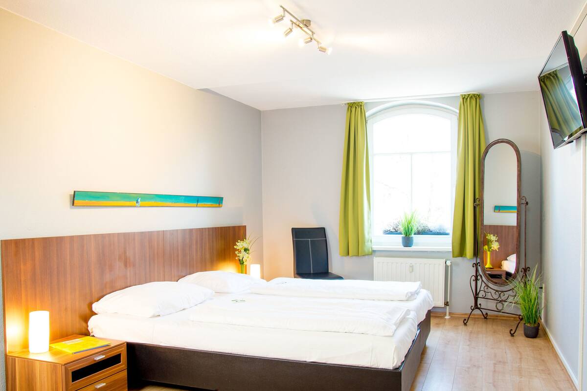 A hotel room with a bed, bedside table, lamp, and a window with curtains.