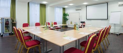 A conference room with a long table, red chairs, a projector screen, and a whiteboard.