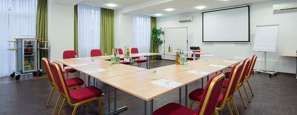 A conference room with a long table, red chairs, a projector screen, and a whiteboard. - Hotel Dampfmühle (Neukirchen-Vluyn)