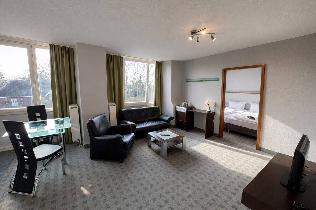 A hotel room with a bed, a desk, a chair, a sofa, and a TV.