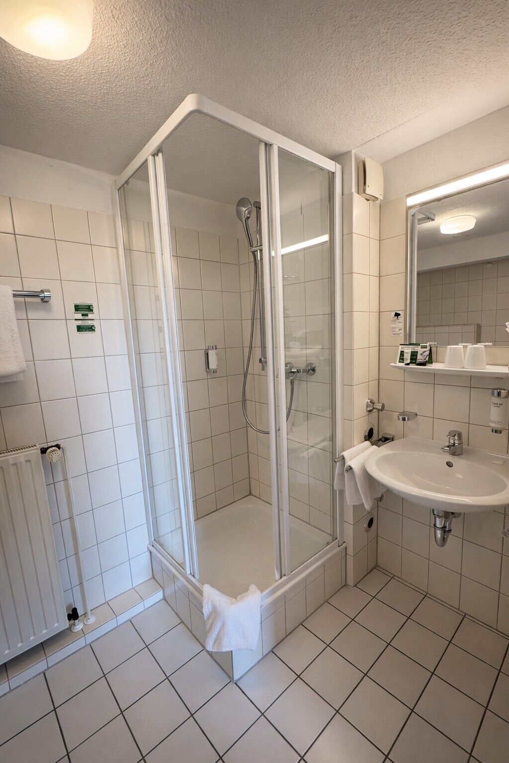 Uma casa de banho moderna com chuveiro envolto em vidro, uma pia branca e um espelho.