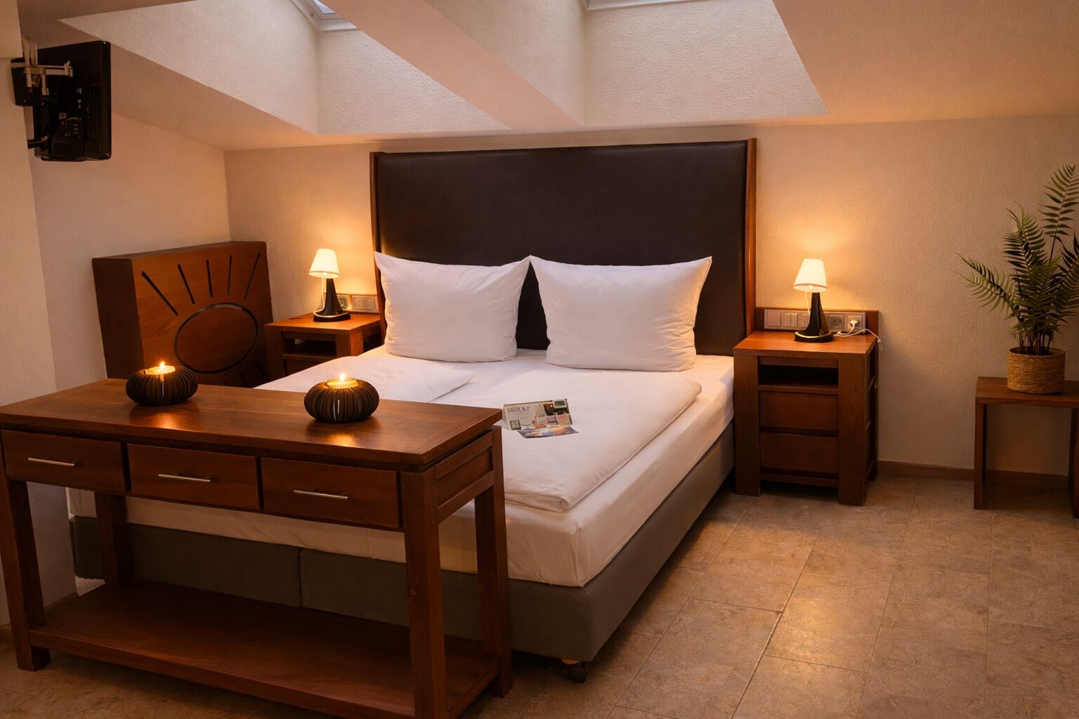 Una habitación de hotel con cama, mesitas de noche, escritorio y una planta en maceta.