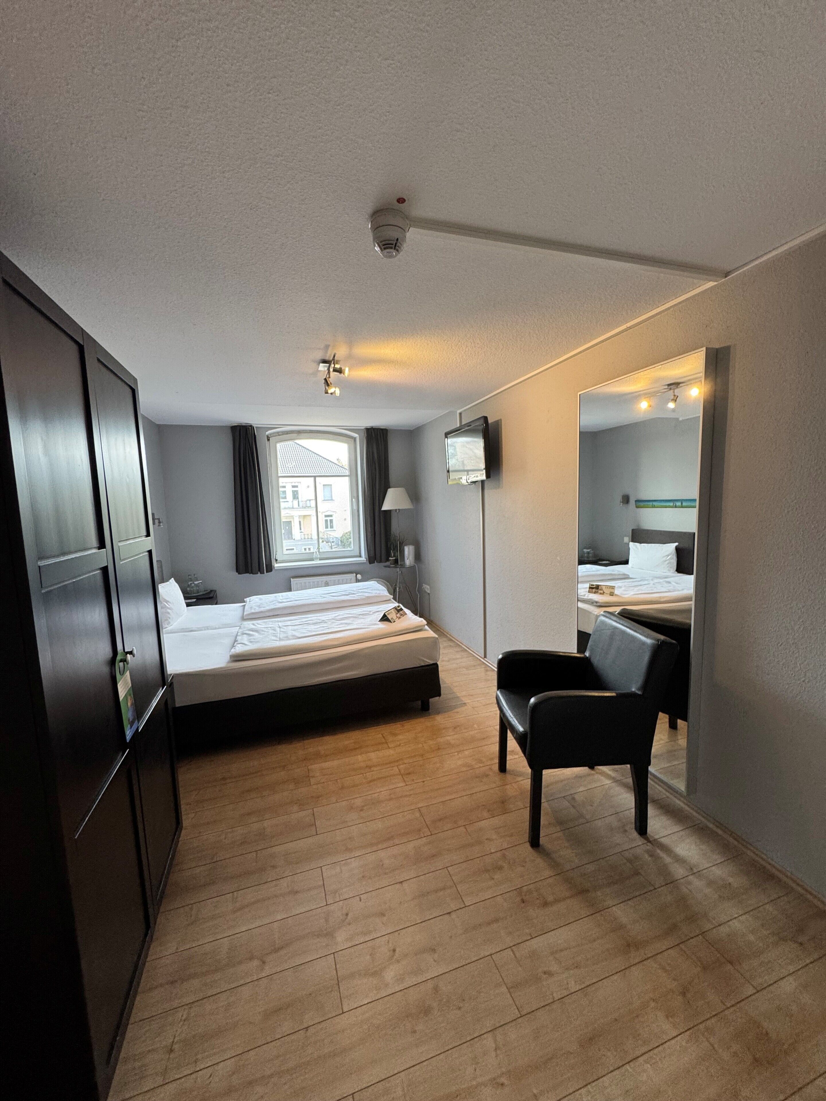 Habitación de hotel con cama, escritorio, silla, televisión y ventana con vista a edificios.