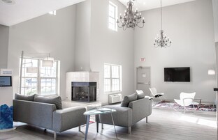 Un salón amplio con sofás grises, una mesa de centro de vidrio, una chimenea y un candelabro.
