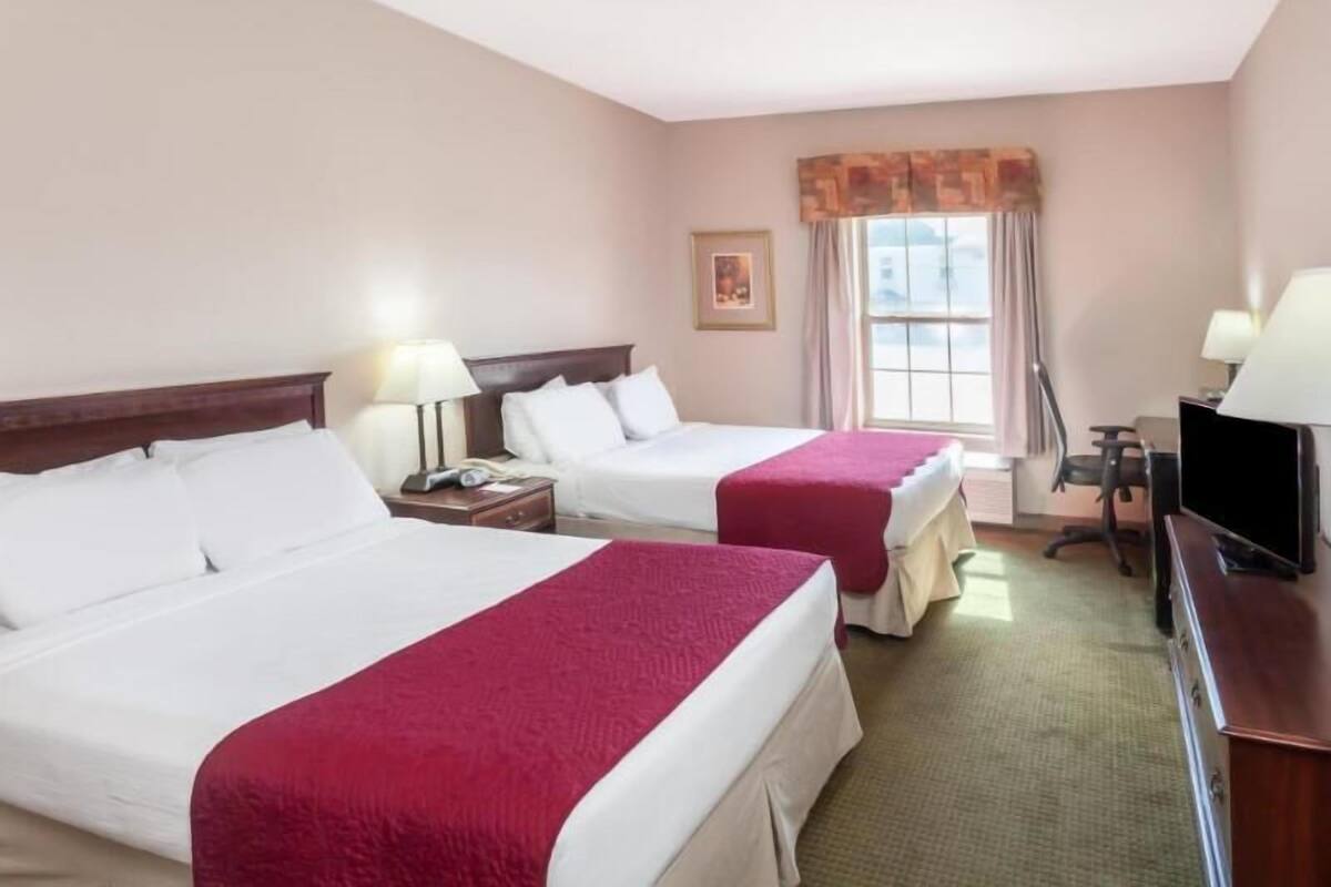 Une chambre d’hôtel avec deux lits, une télévision, un bureau et une fenêtre avec des rideaux.
