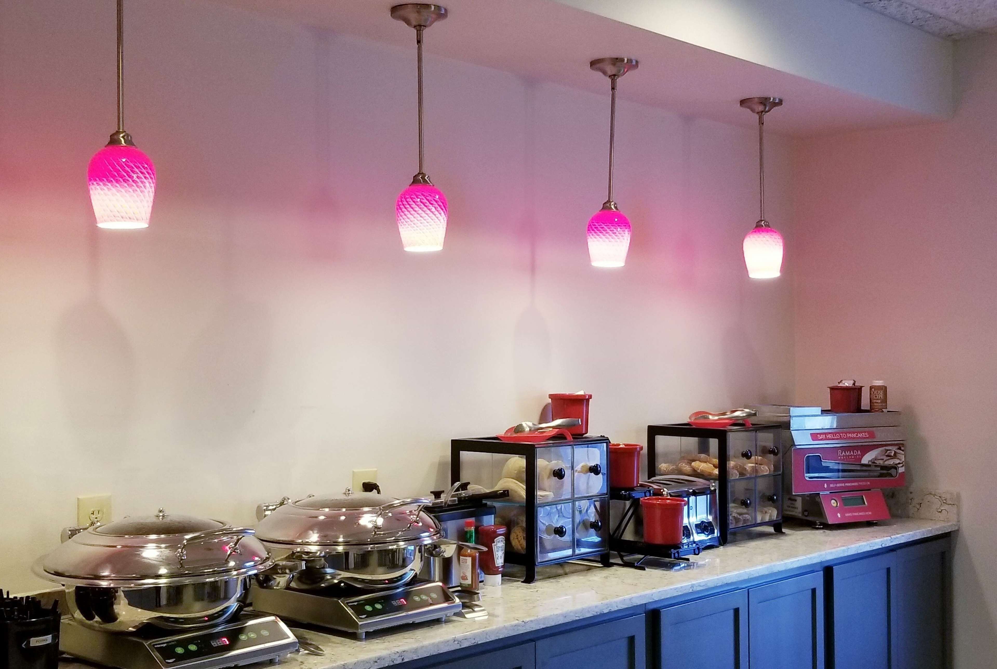 A kitchen with four hanging pendant lights, a countertop with various kitchen appliances and containers, and a wall-mounted spice rack.