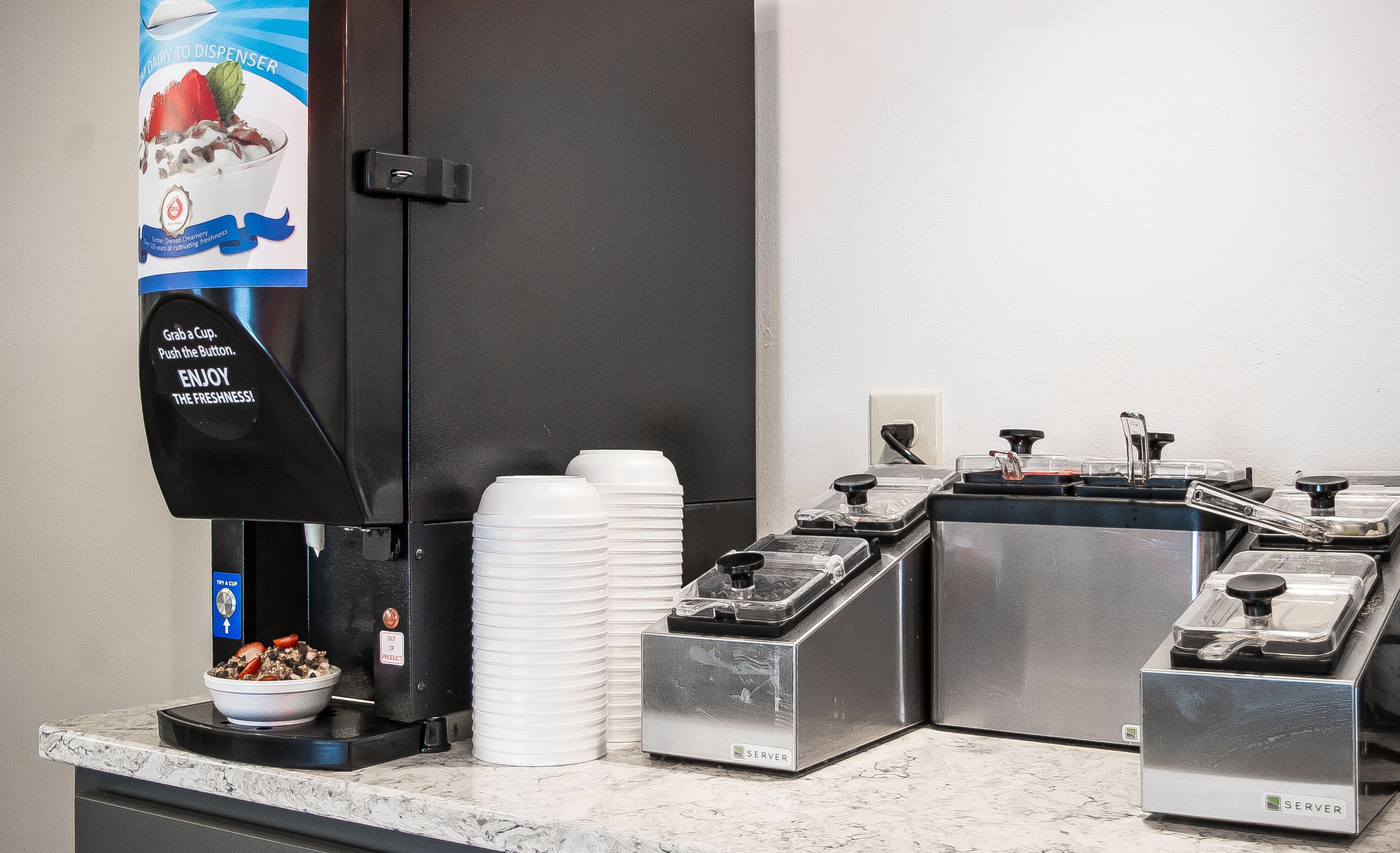 Een koffiehoek waar je zelf je koffie kunt maken, met een melkdispenser, wegwerpbekers en een kommetje eten.