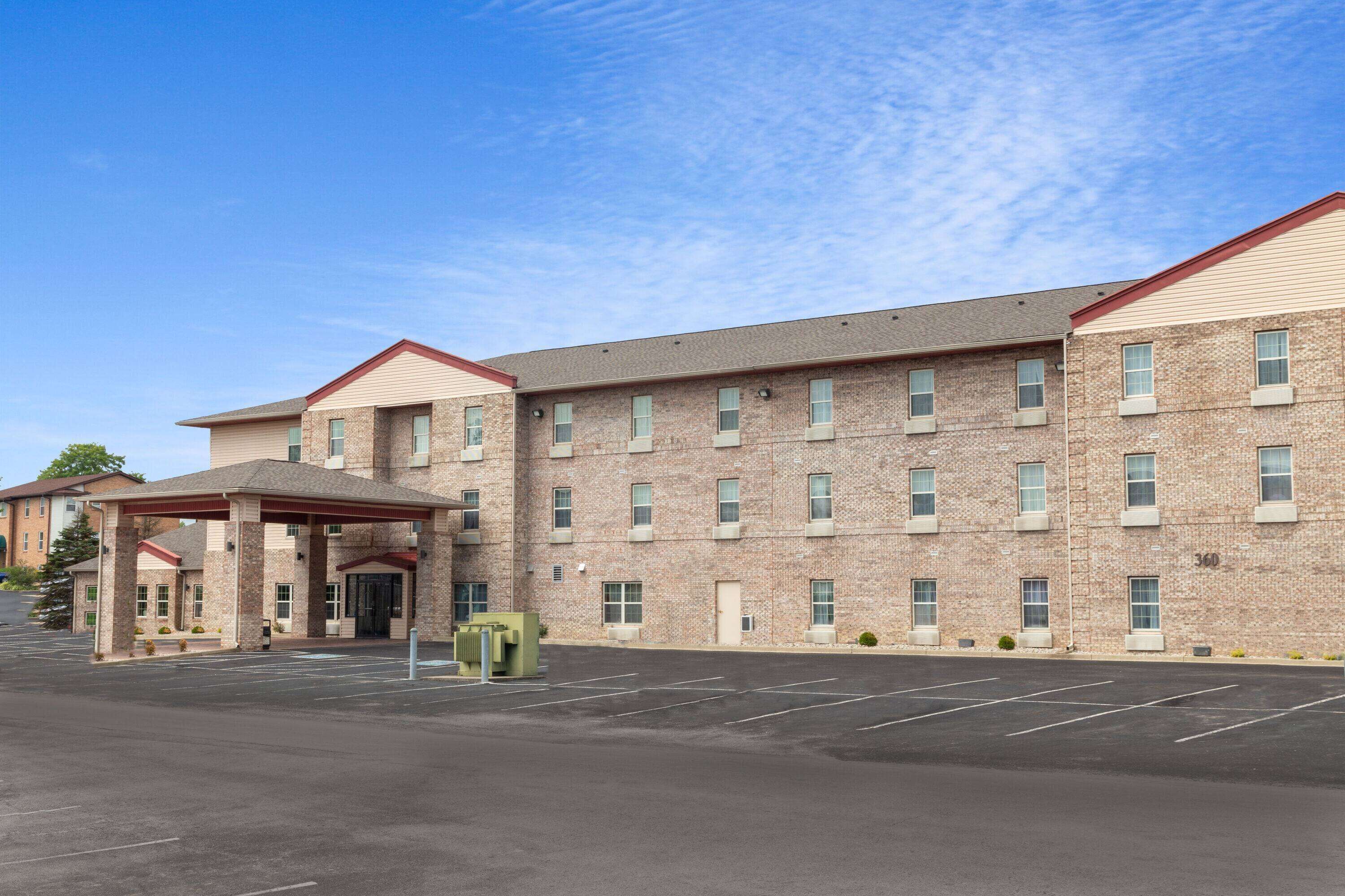A multi-story hotel with a brick facade, a covered entrance, and a parking lot.
