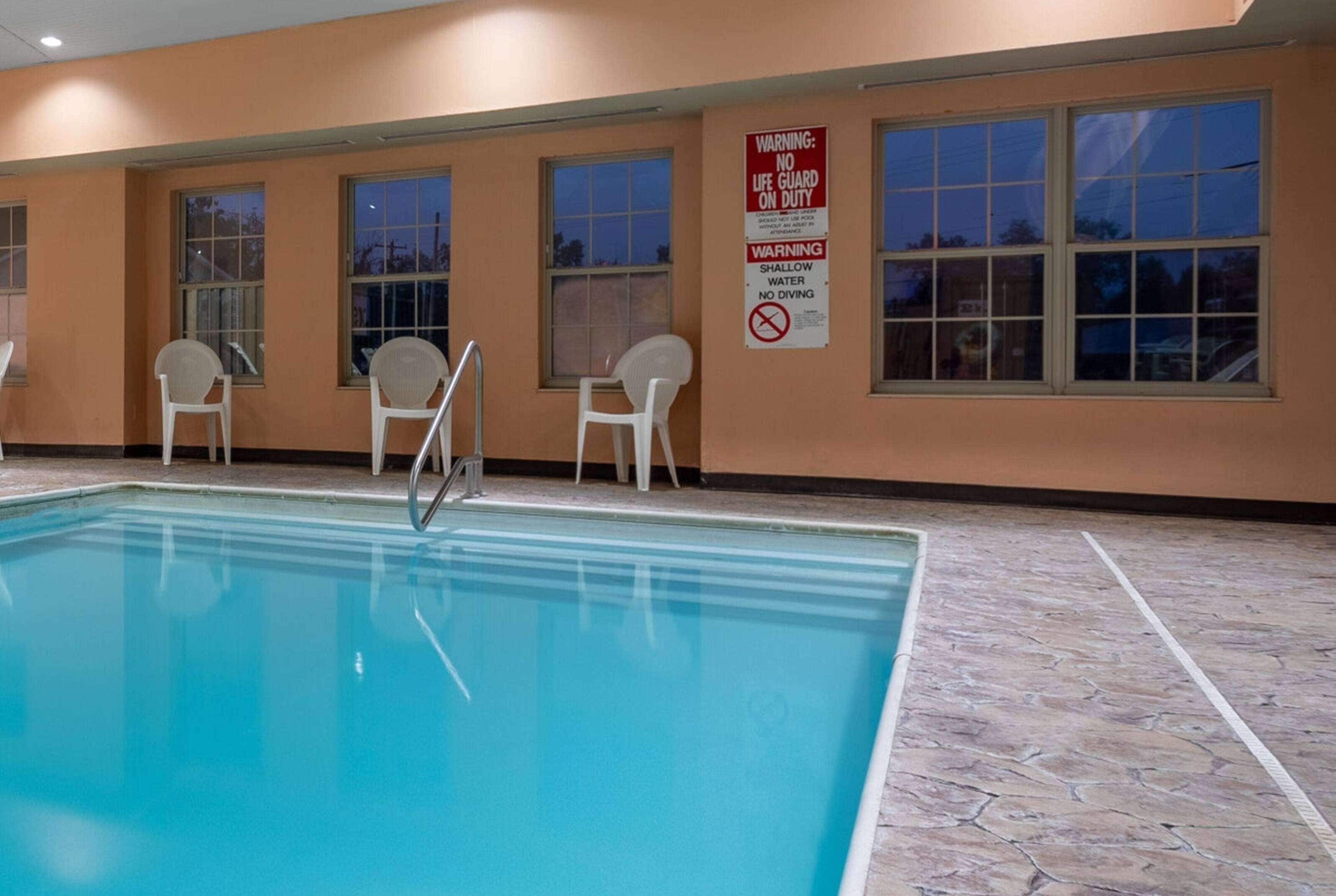 Una piscina interior con una silla de socorrista, señales de advertencia y suelo de baldosas.