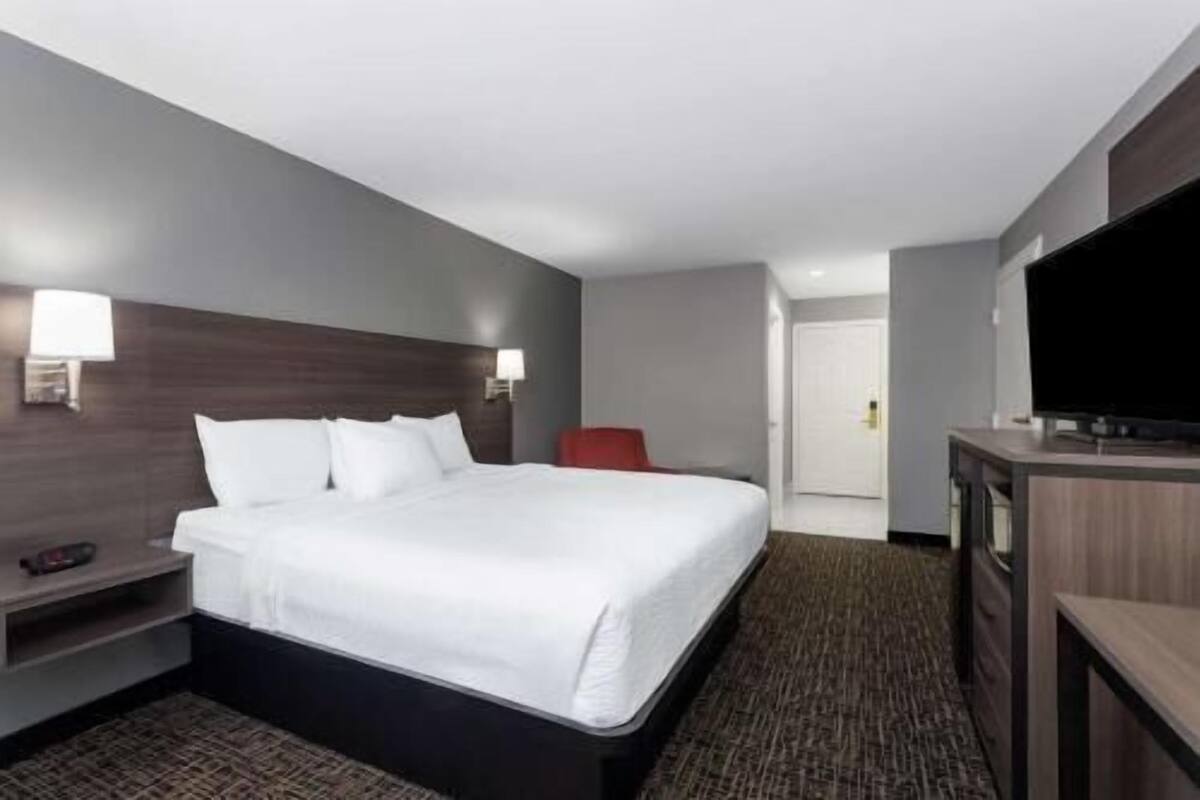 Quarto de hotel com cama, mesas de cabeceira, televisão e porta.