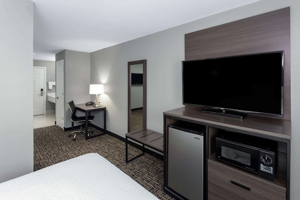 A hotel room with a bed, desk, chair, TV, refrigerator, and microwave.