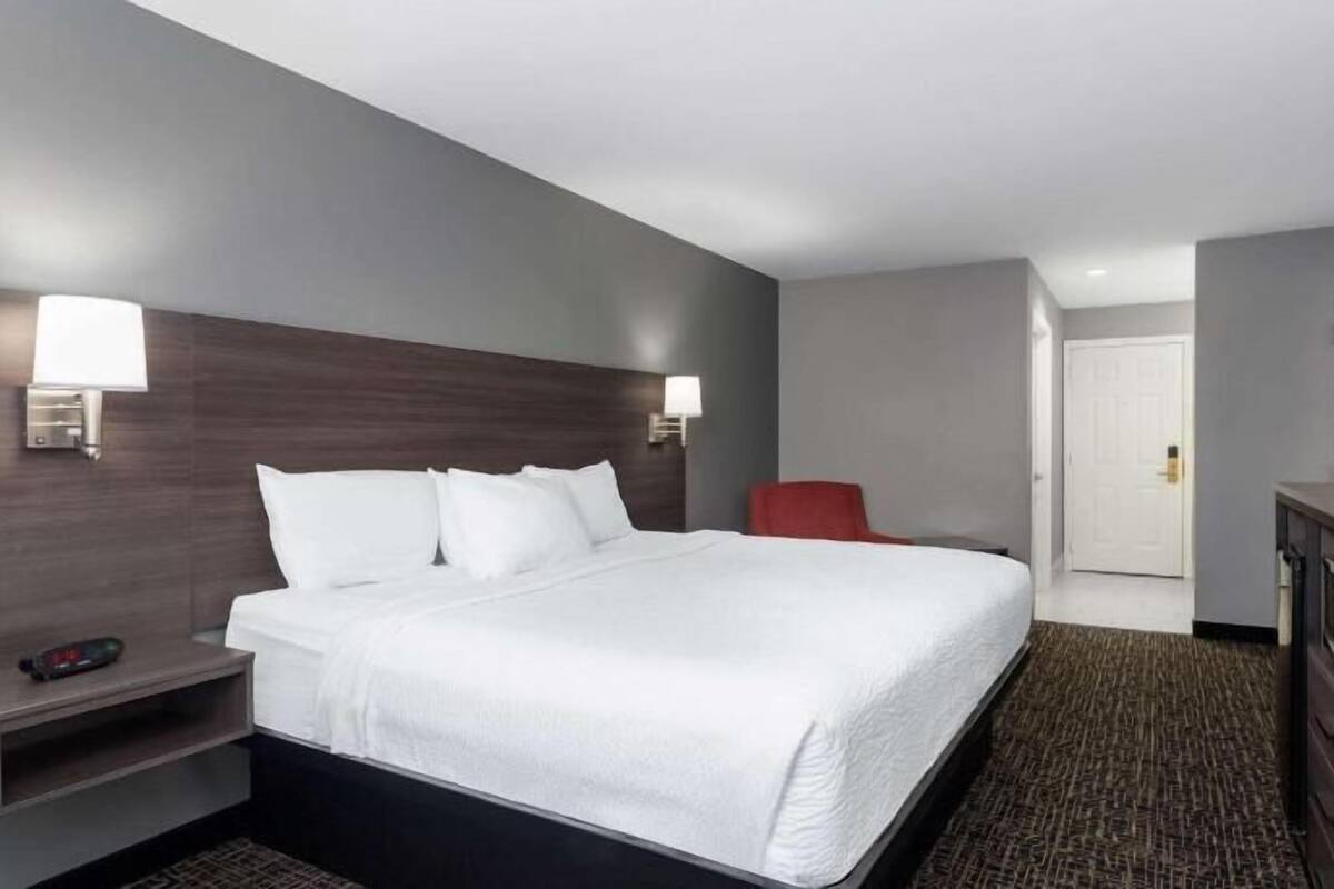 Quarto de hotel com cama, mesas de cabeceira, televisão e uma cadeira vermelha.