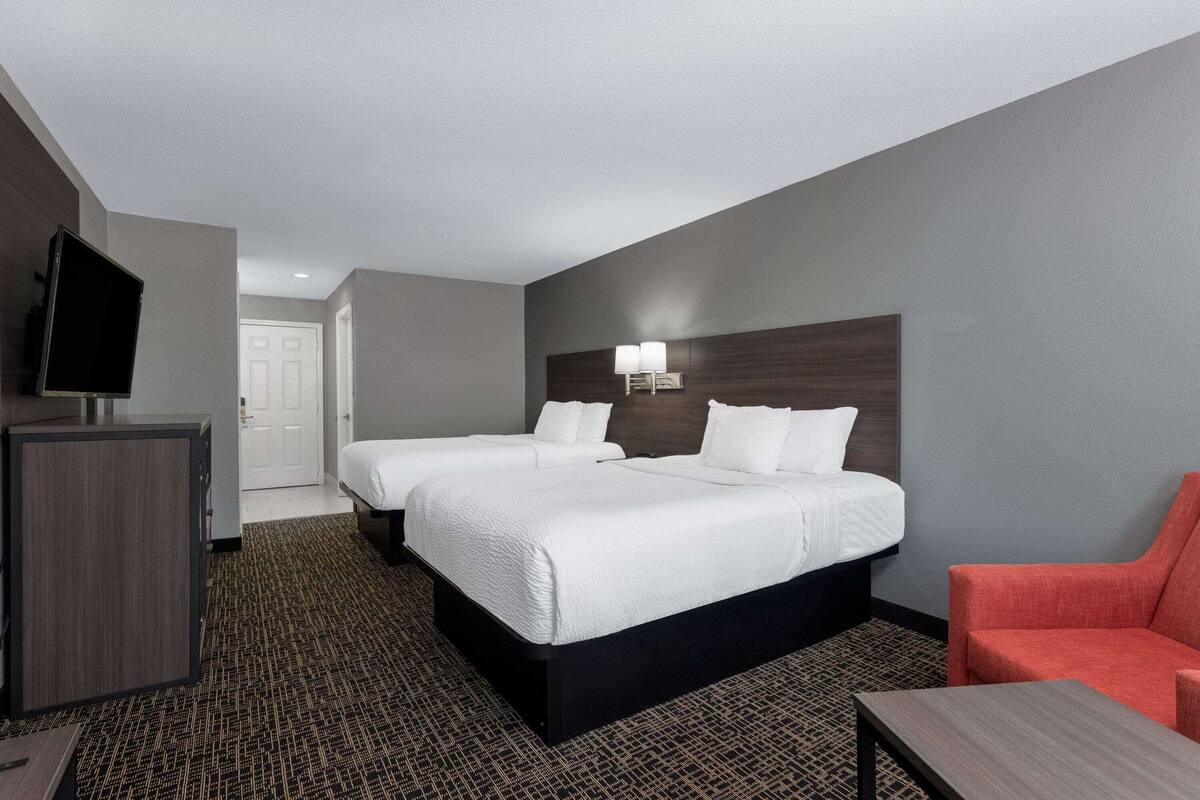 Quarto de hotel com duas camas, uma escrivaninha, uma televisão e uma cadeira vermelha.