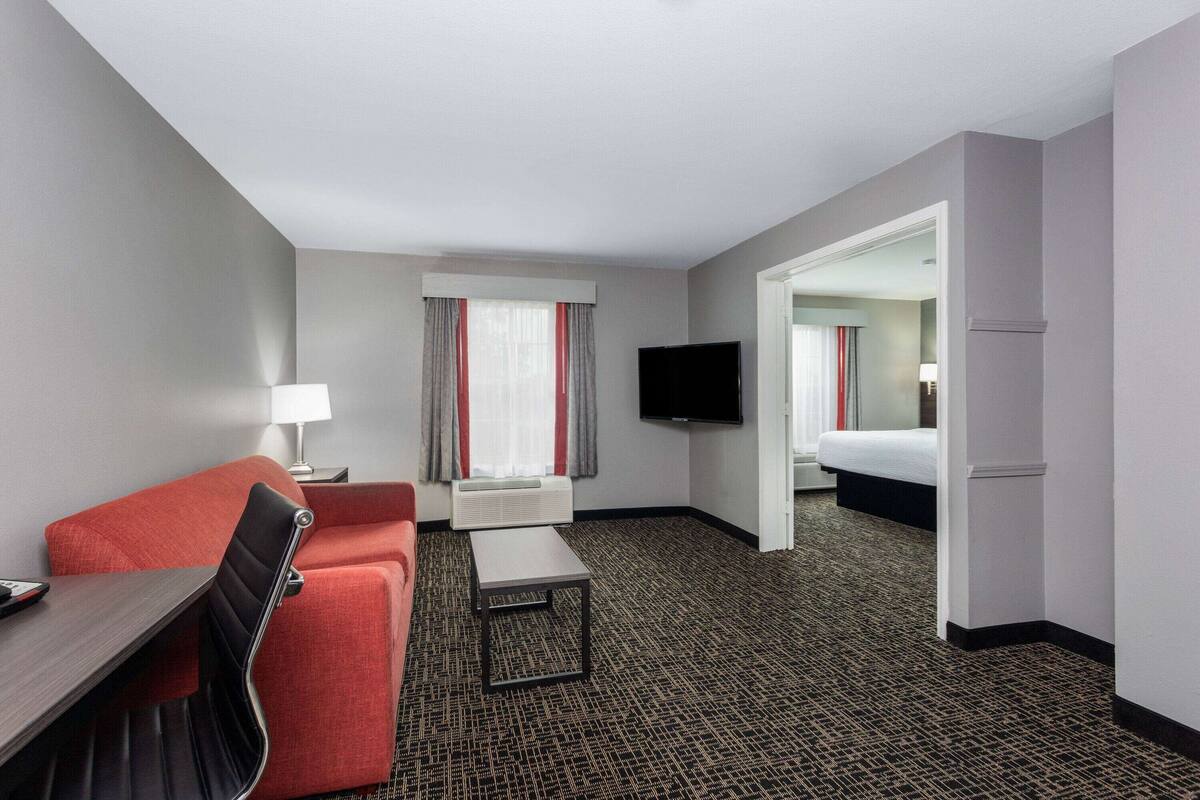Quarto de hotel com sofá vermelho, uma mesinha, televisão e cama.
