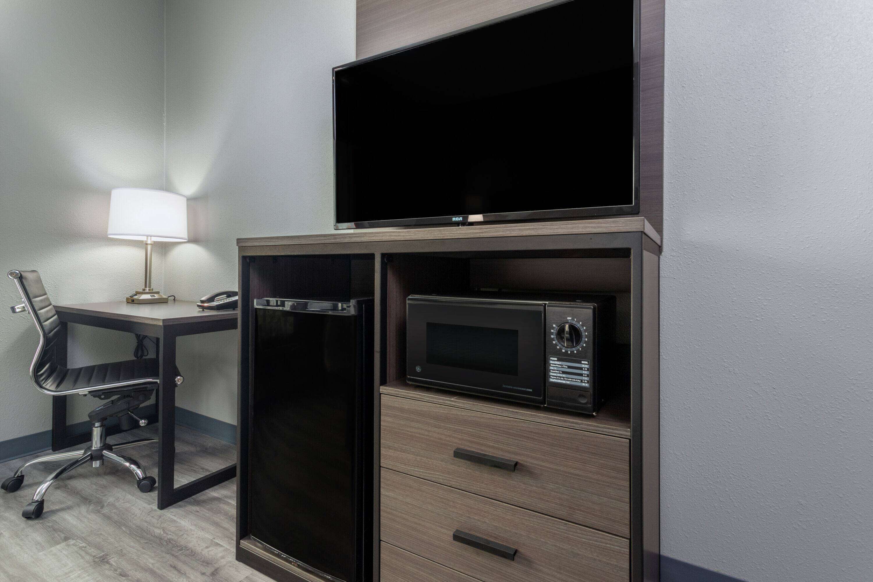 A compact hotel room with a desk, a chair, a television, and a microwave.