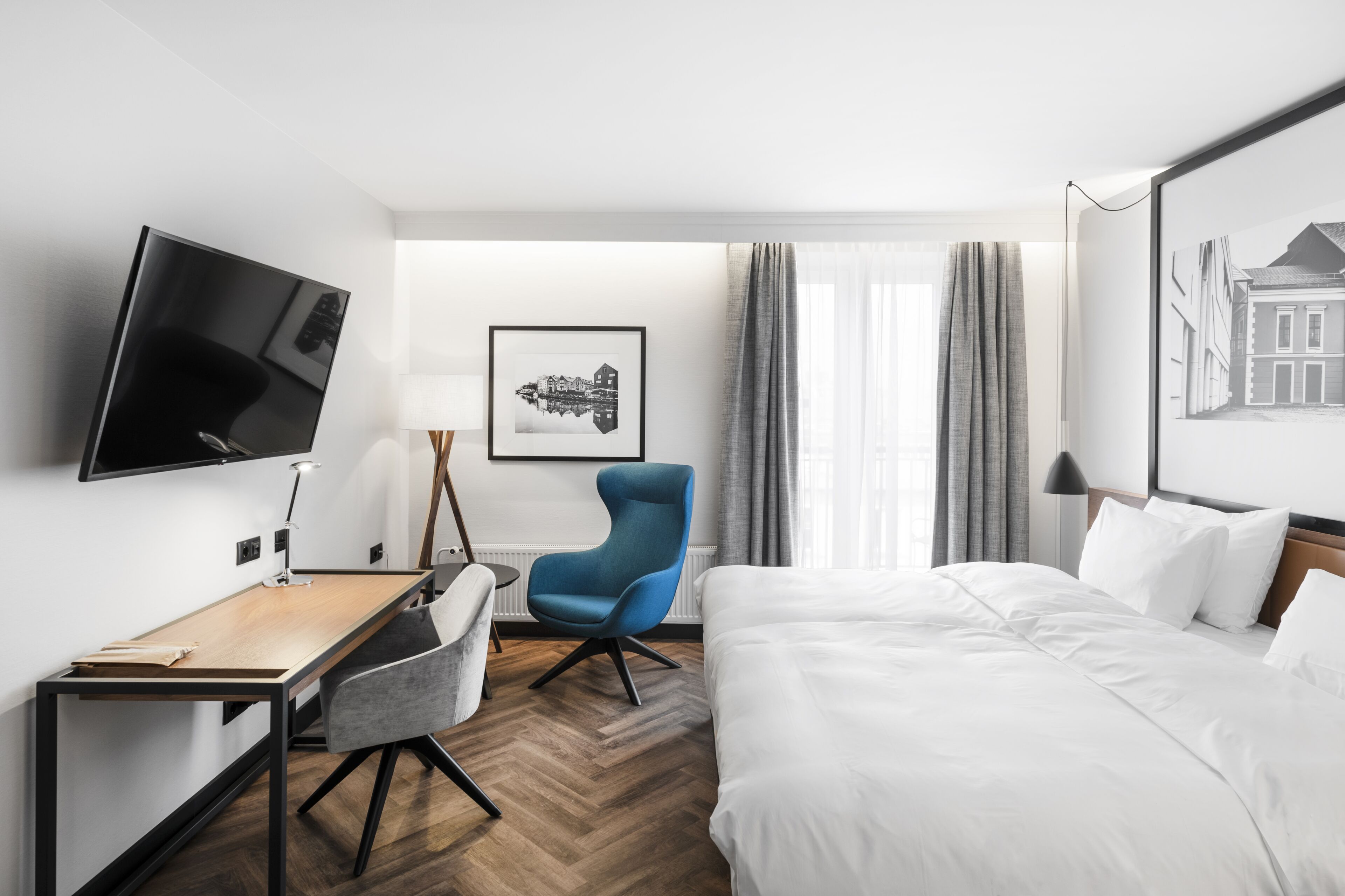 A hotel room with a bed, a desk, a chair, a TV, and a framed picture on the wall.