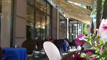 Un espace extérieur aménagé avec des tables et des chaises, une paroi en verre et une partie couverte.