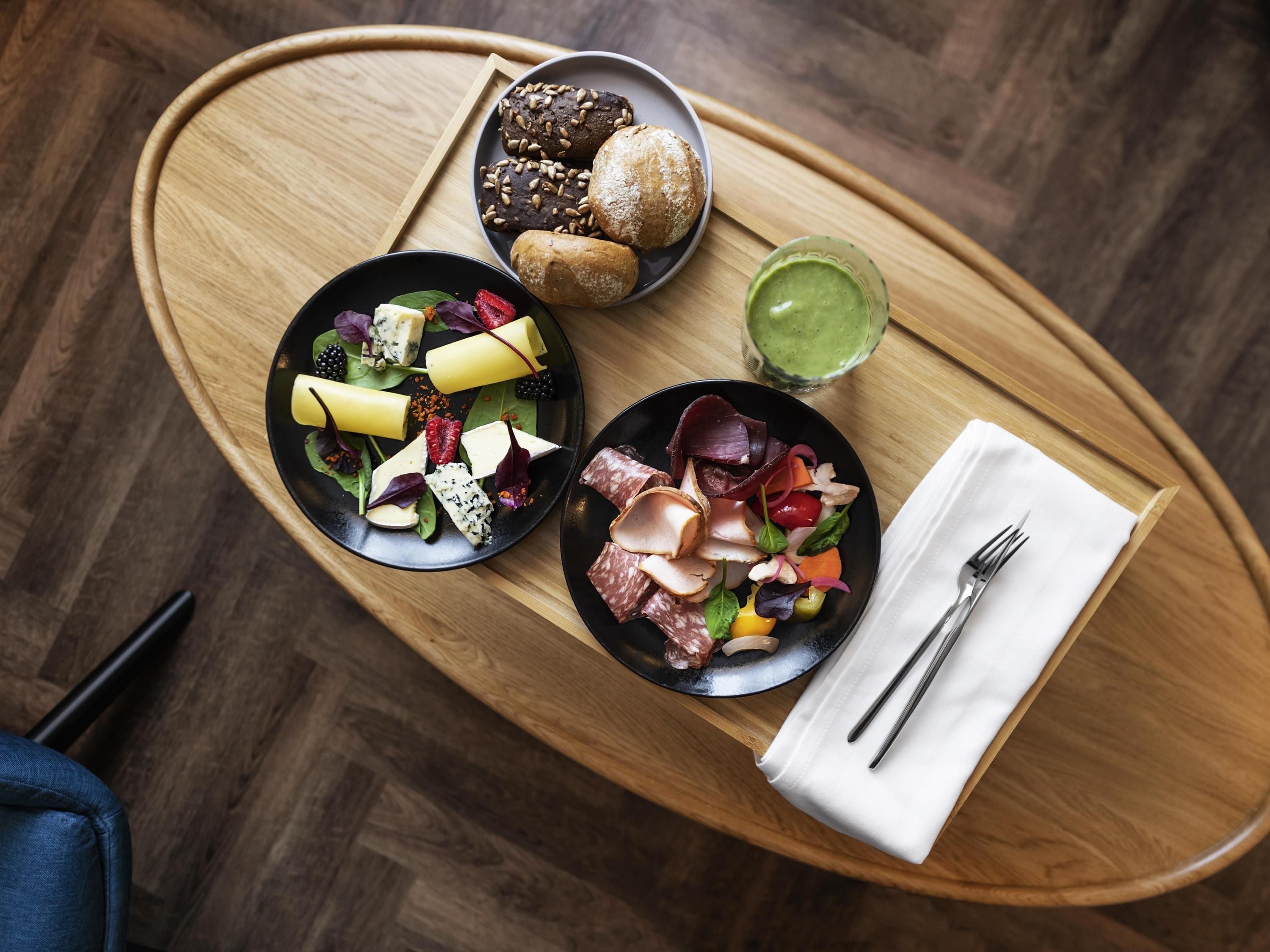 A wooden tray with two plates of food, a bowl of soup, and a glass of green sauce.