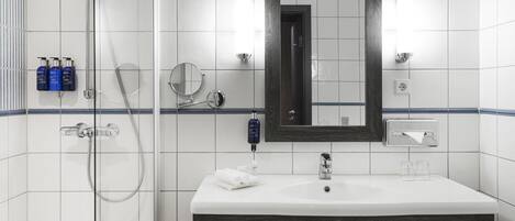 A modern bathroom with a white sink, dark wood vanity, a glass shower enclosure, and a mirror above the sink.