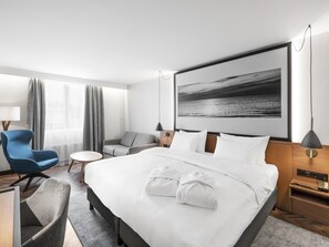 Ein Hotelzimmer mit einem großen Bett, einem Schreibtisch mit Stuhl, einer Couch und Meerblick.