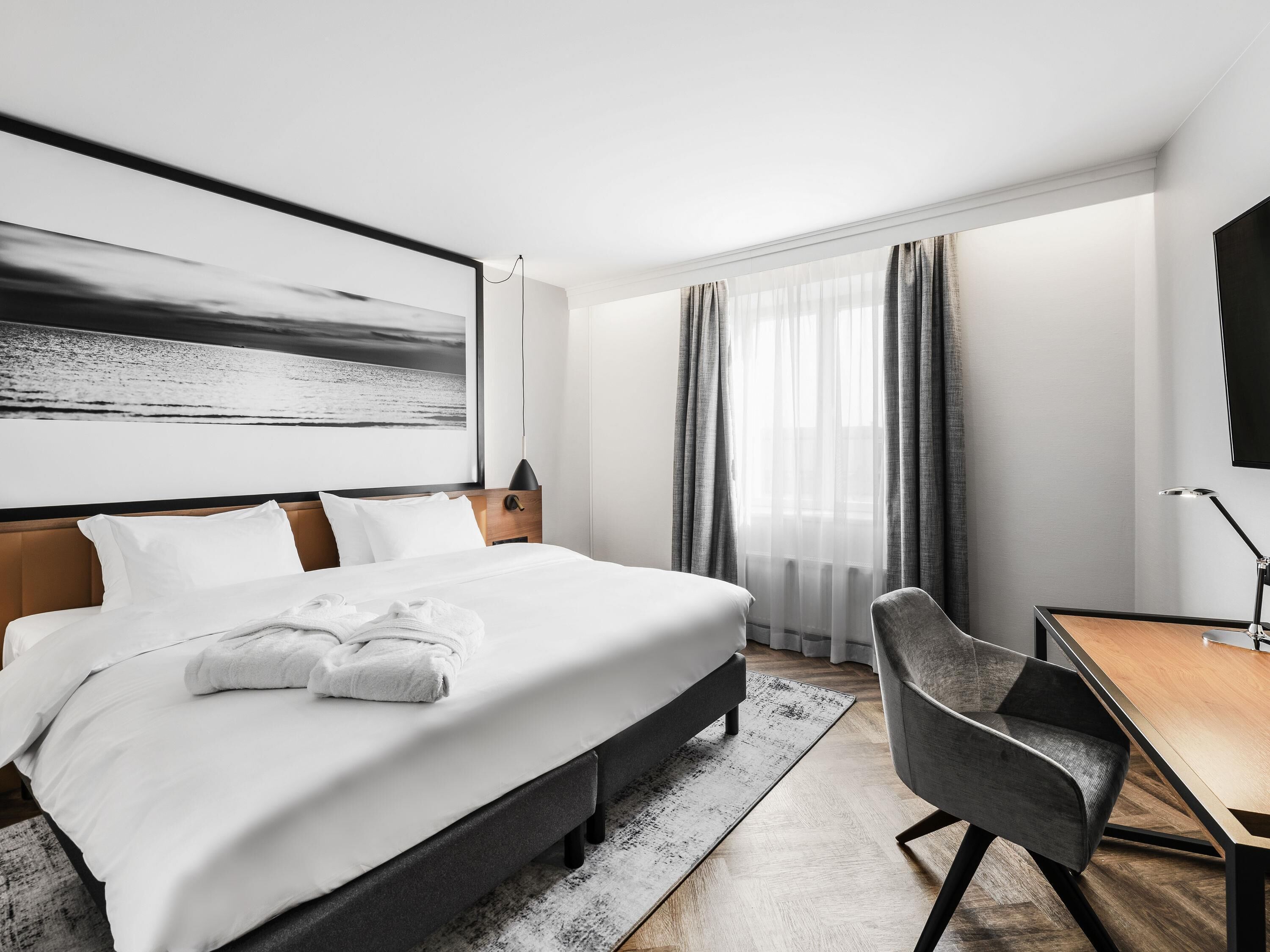 A modern hotel room with a large bed, a desk, and a view of the sea.