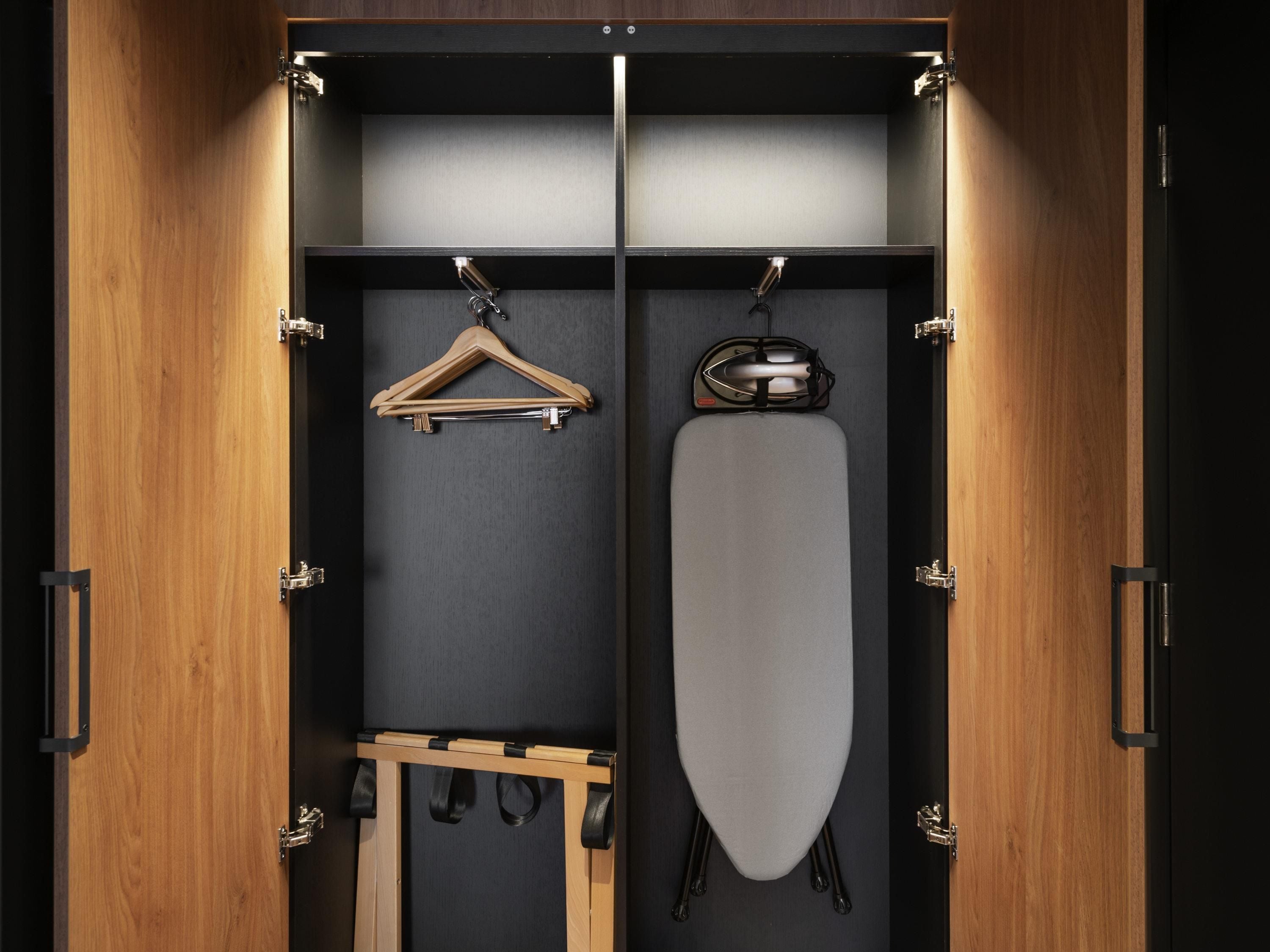 A wardrobe with a wooden interior, featuring a hanging rack, a mirror, and a hanging garment bag.