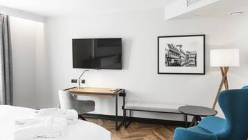 Una habitación de hotel con una cama, un escritorio con una silla, un televisor, un cuadro enmarcado, una lámpara y un sillón azul.