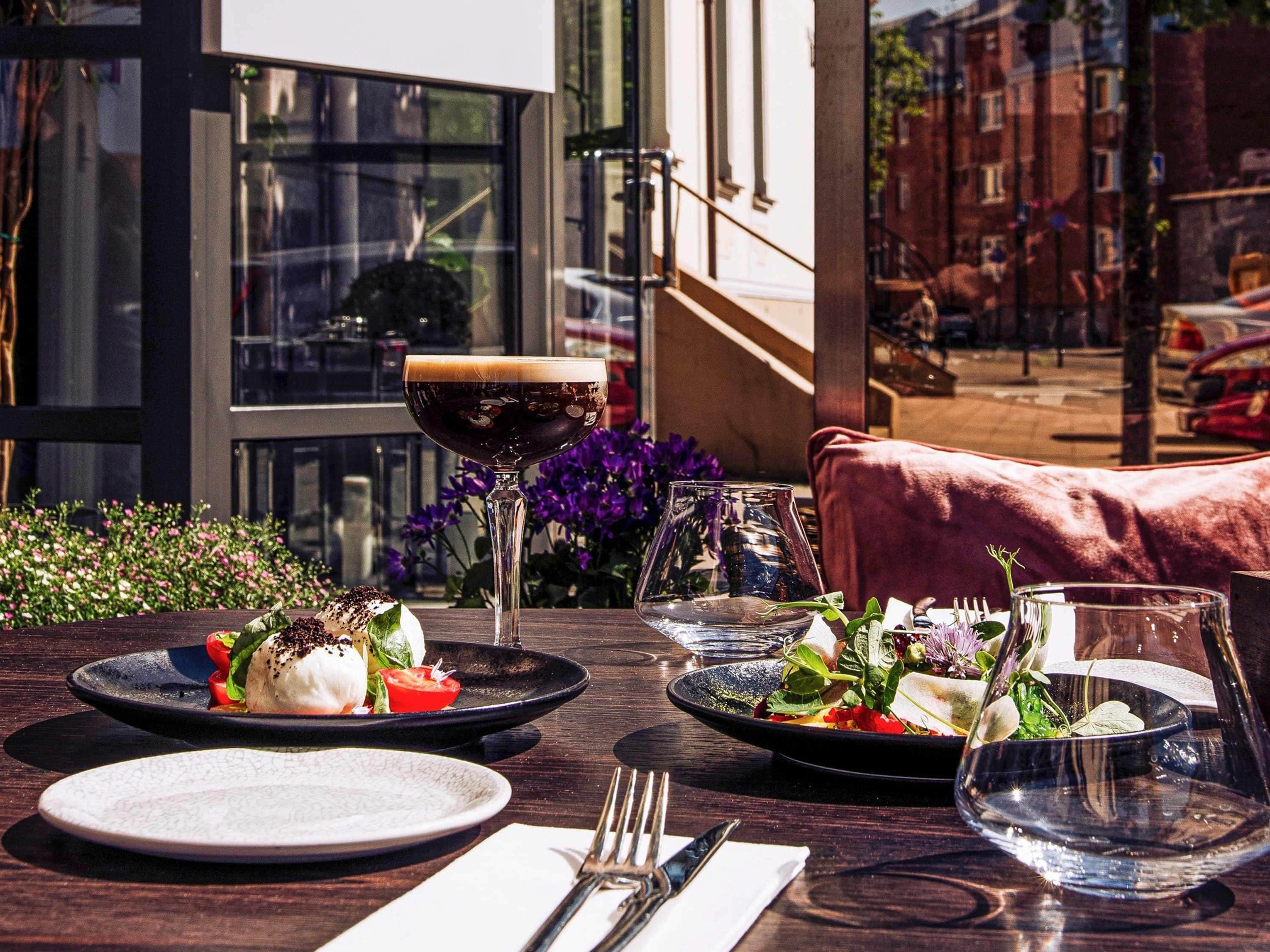 An outdoor dining area with a table set for two, featuring plates of food, a glass of red wine, and a glass of water.