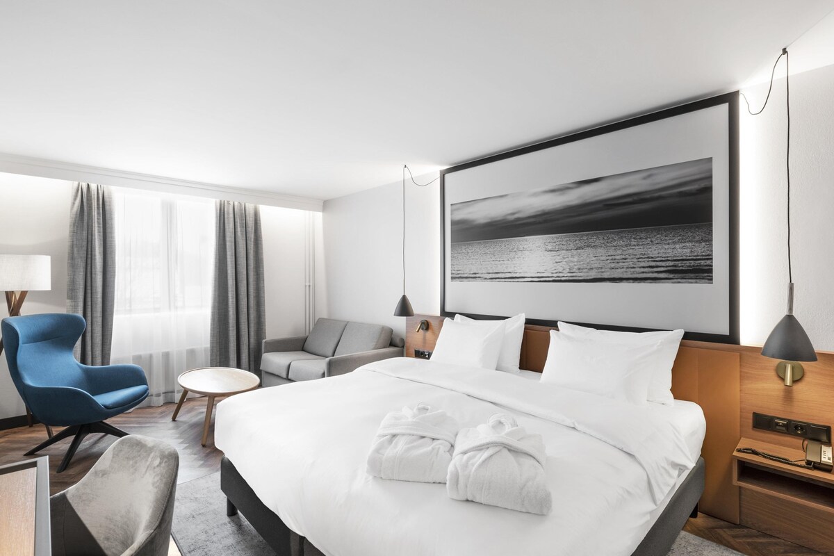 Habitación de hotel con una cama grande, un escritorio con silla, un sofá y vista al mar.