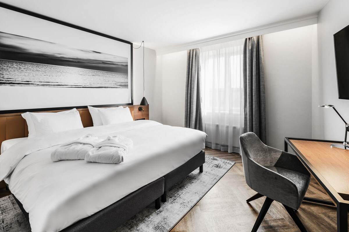 Una habitación de hotel moderna con una cama grande, un escritorio y vistas al mar.