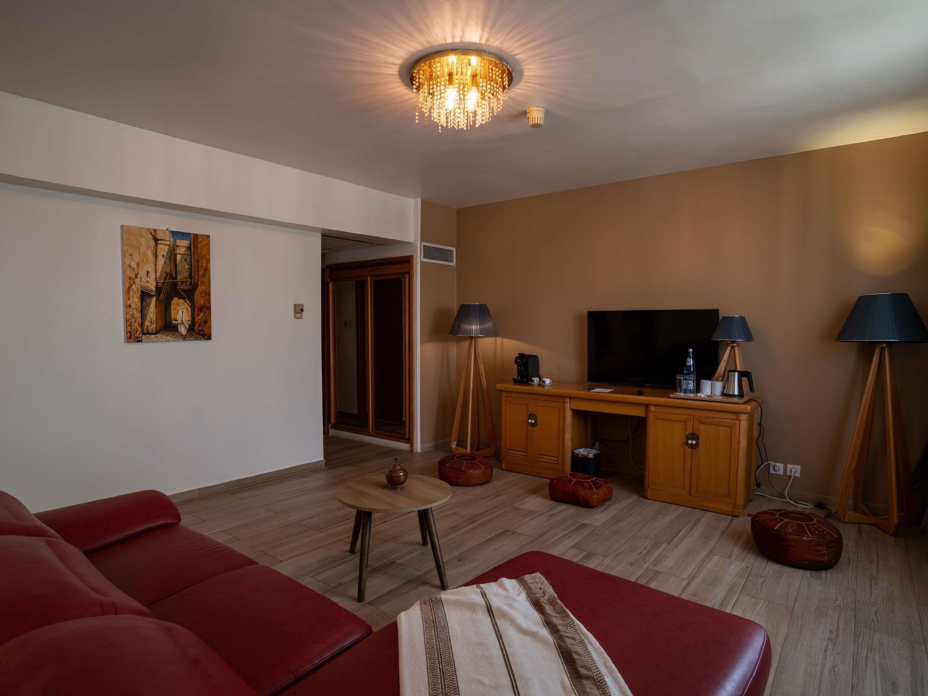 A living room with a red sofa, a wooden entertainment unit, a television, and a chandelier.