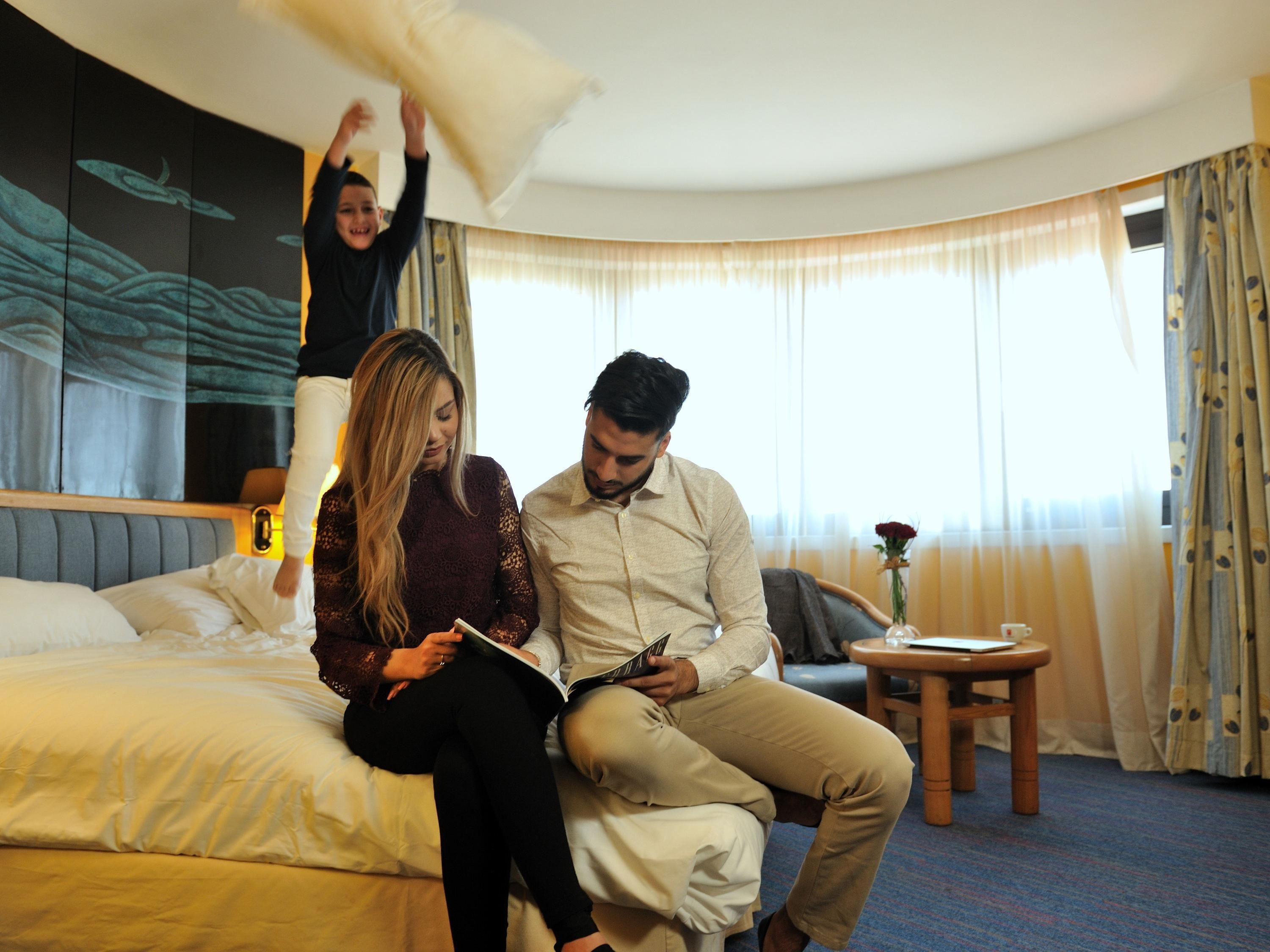A hotel room with a bed, a small table, and a window with curtains.