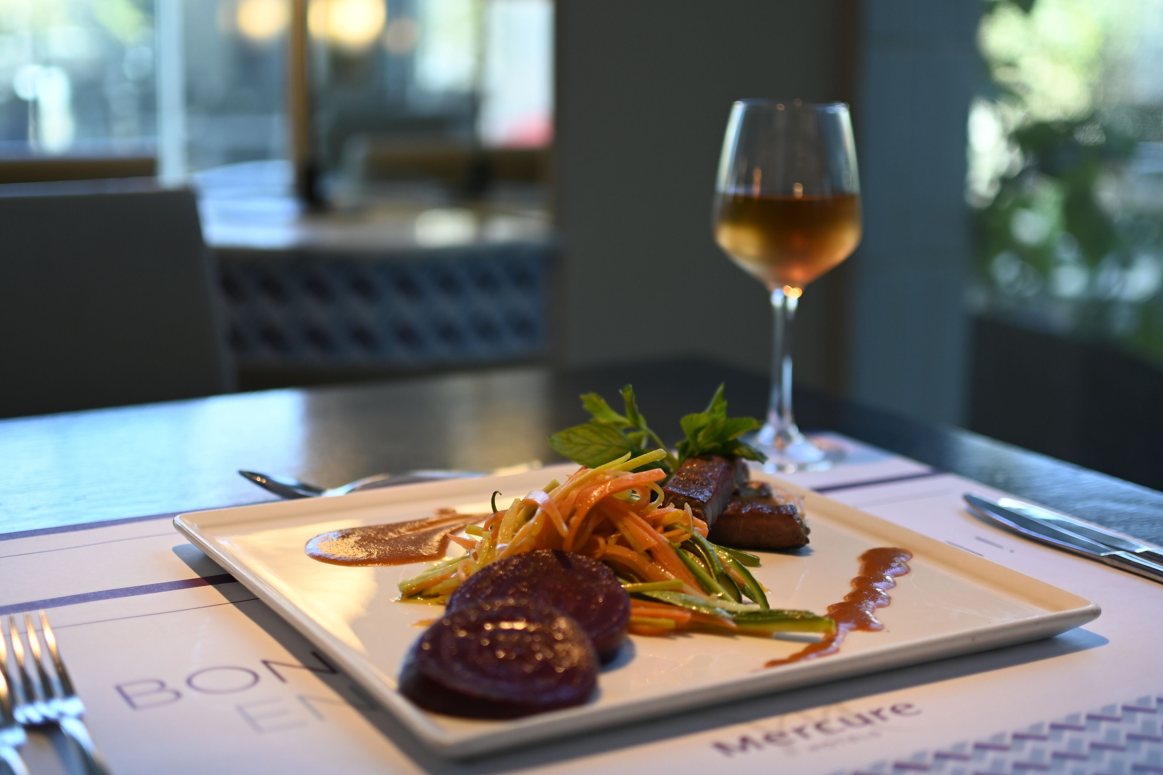 A dining table with a plate of food, a glass of wine, and cutlery.