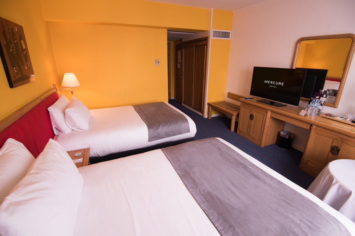 A hotel room with two beds, a television, a desk, and a mirror.