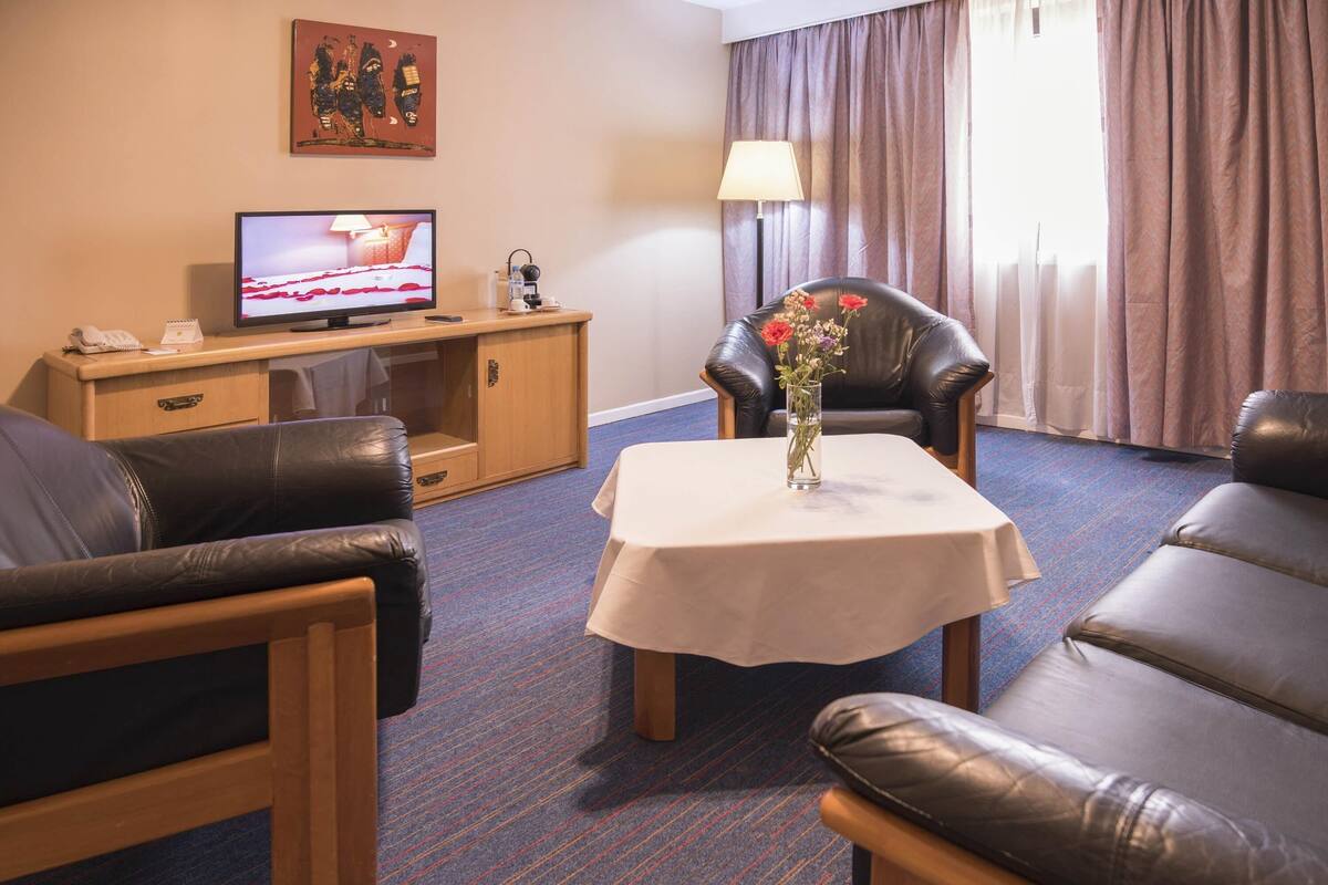 A hotel room with leather sofas, a television, a small table with a vase, and a cabinet with a lamp.