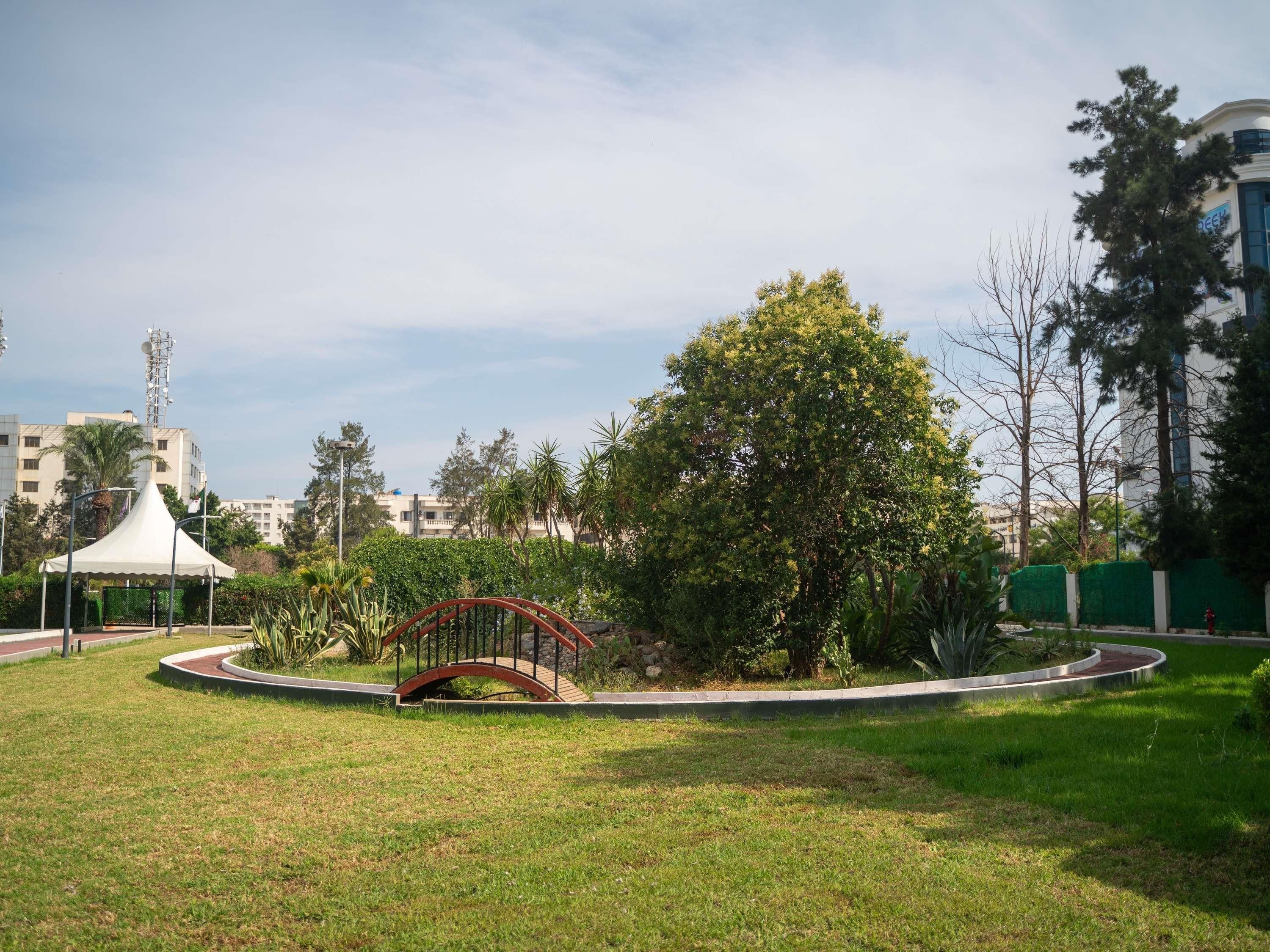 A park with a red bridge, a white tent, and a large tree.