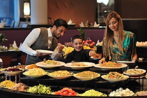 A buffet with various dishes and a man serving food to a child. - Mercure Alger Aeroport (Algiers)