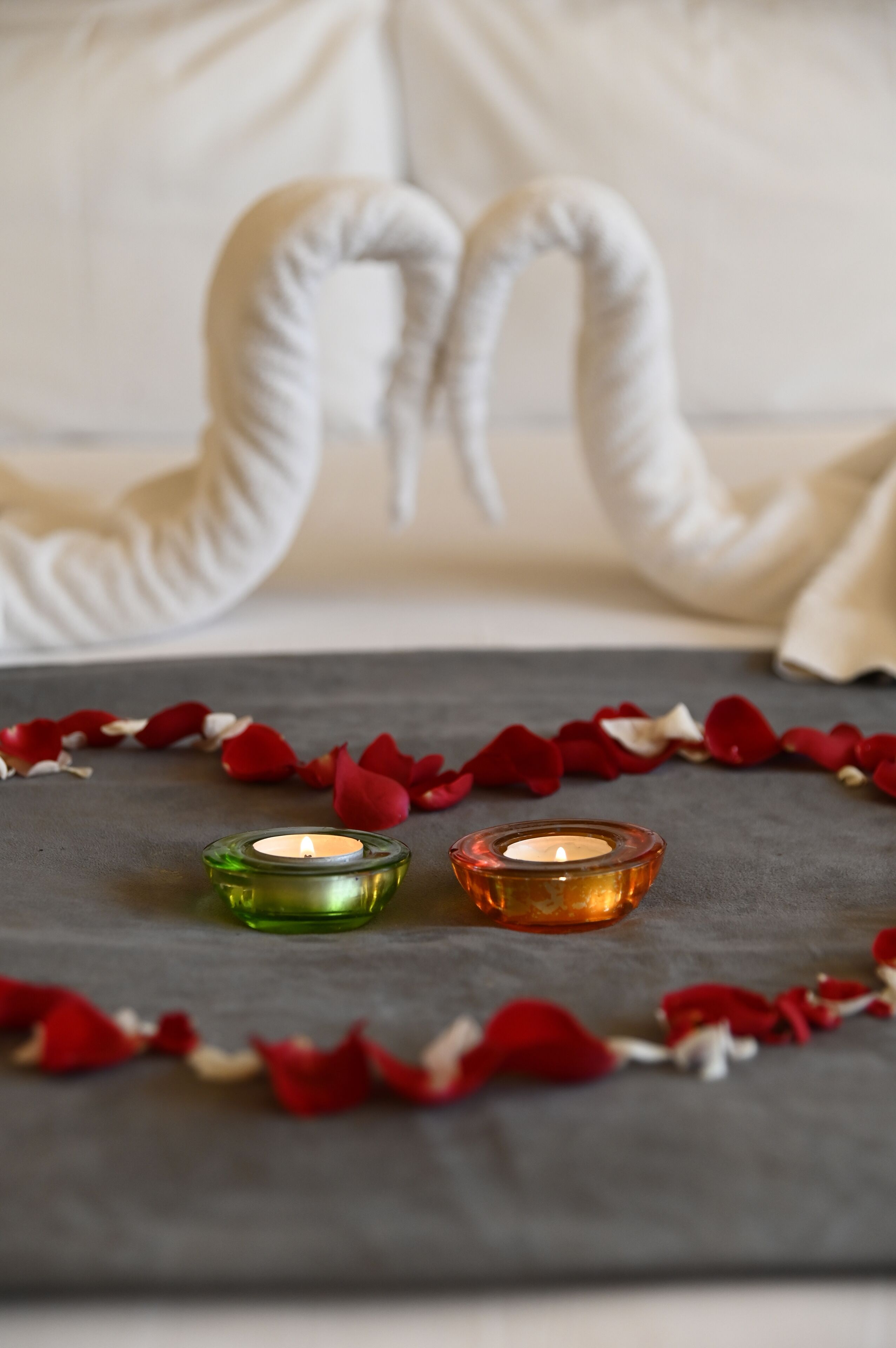 Une table éclairée à la bougie, décorée de pétales de rose et ornée de deux bougies dans des supports verts et orange.