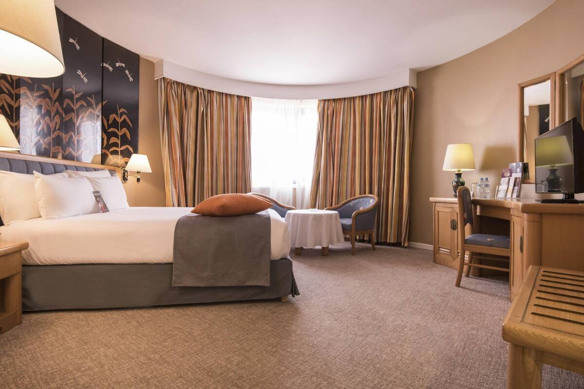 A hotel room with a bed, a desk, a chair, a television, and curtains.