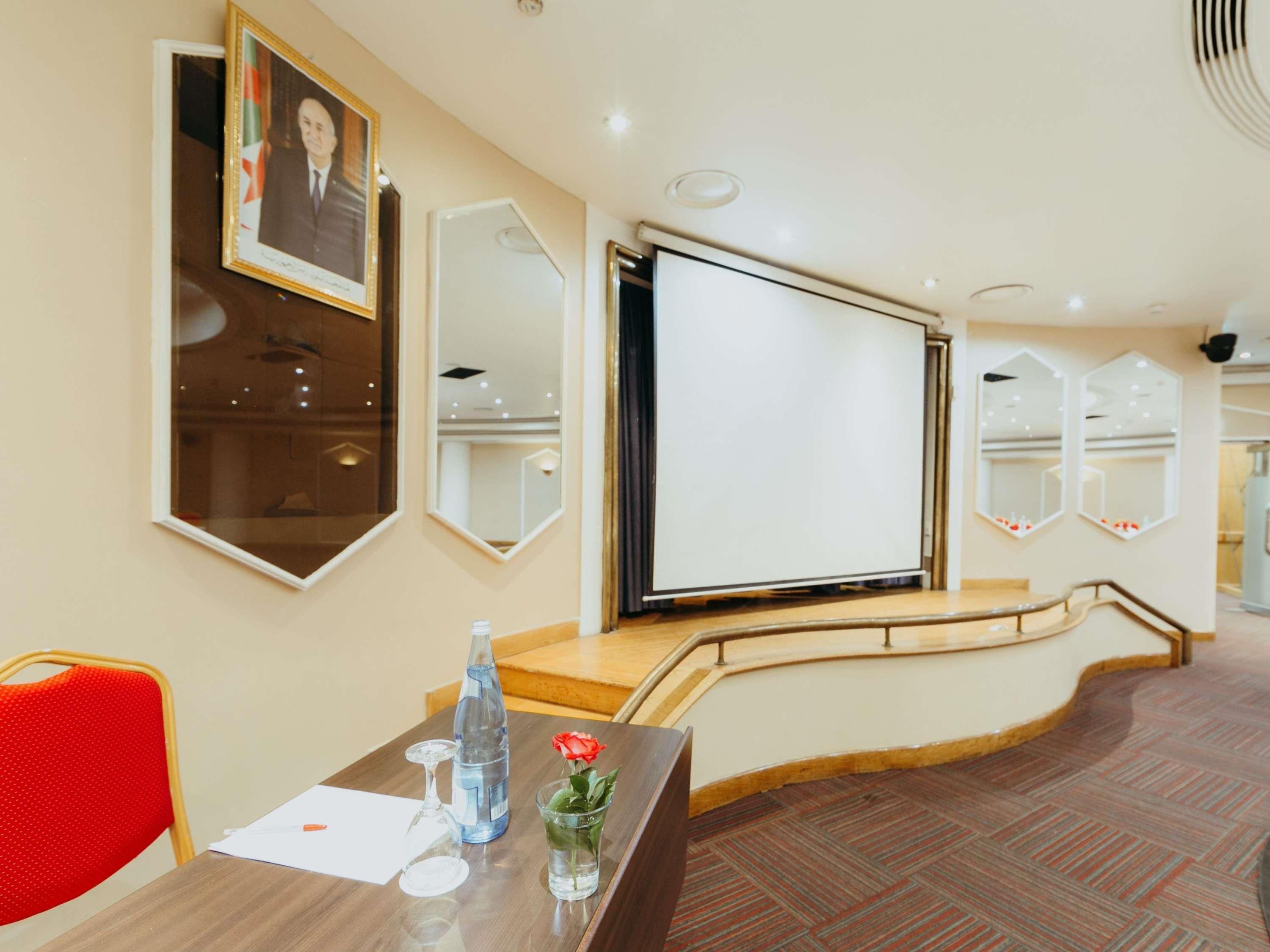 A hotel lobby with a reception desk, a framed portrait, a large mirror, and a staircase.