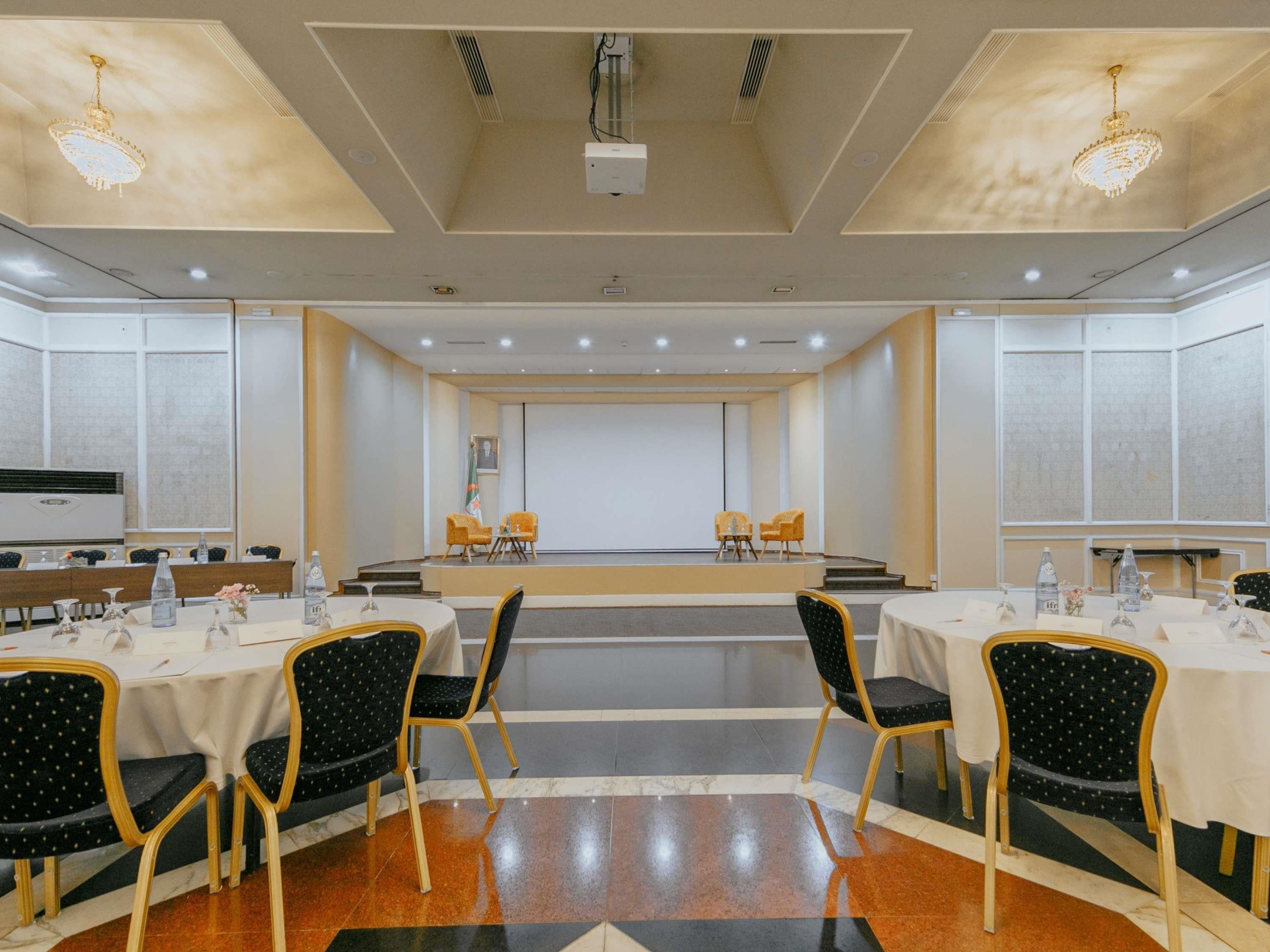 Un salón de conferencias con escenario, varias mesas y sillas.