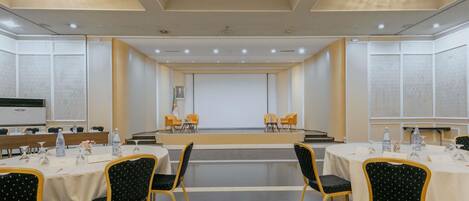 Un salón de conferencias con escenario, varias mesas y sillas.