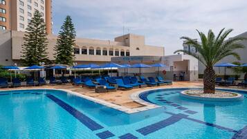 Una piscina al aire libre, sombrillas, sillones reclinables de piscina