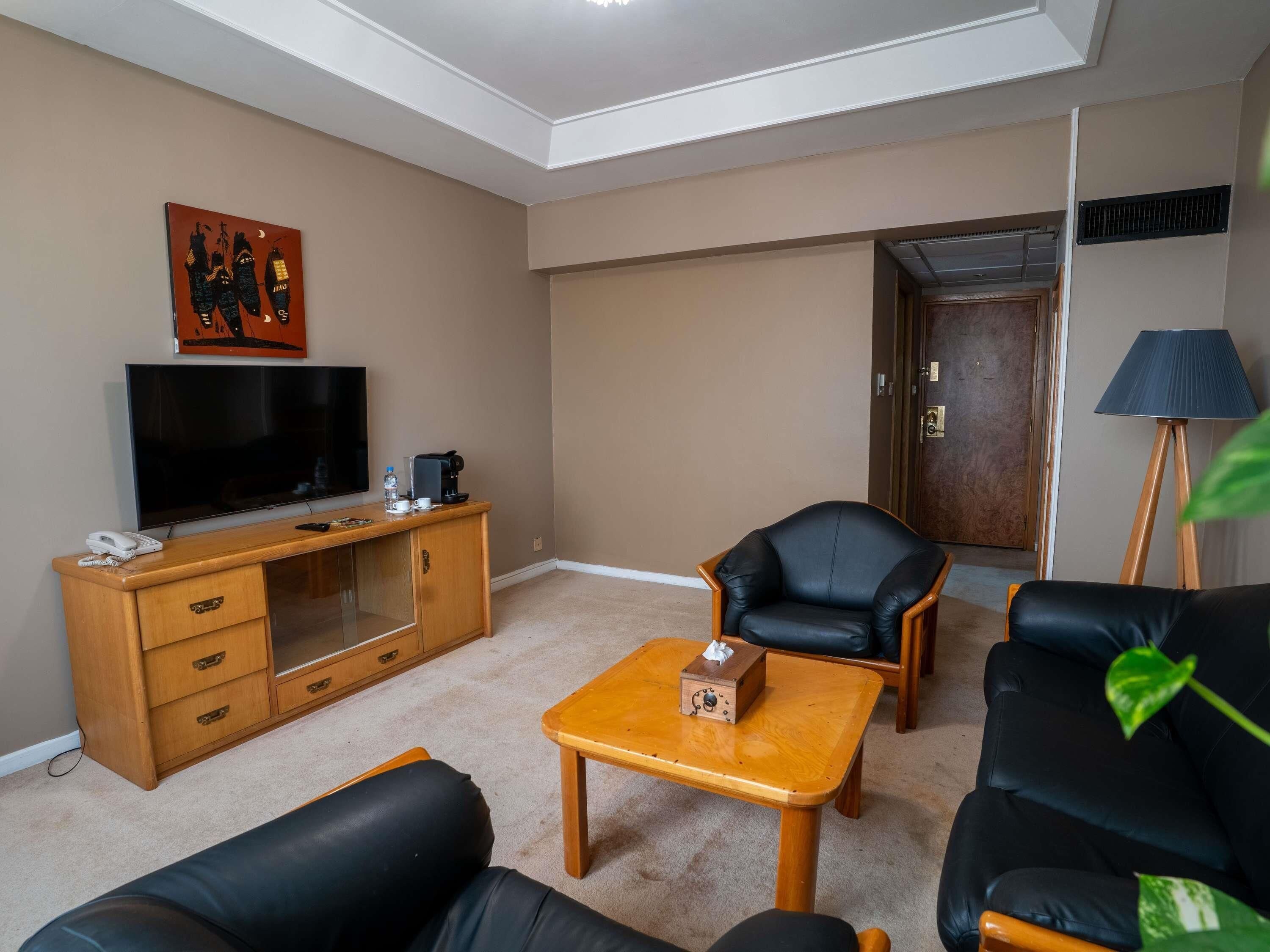 Una sala de estar con televisor, muebles de madera, un sofá de cuero negro y una lámpara.