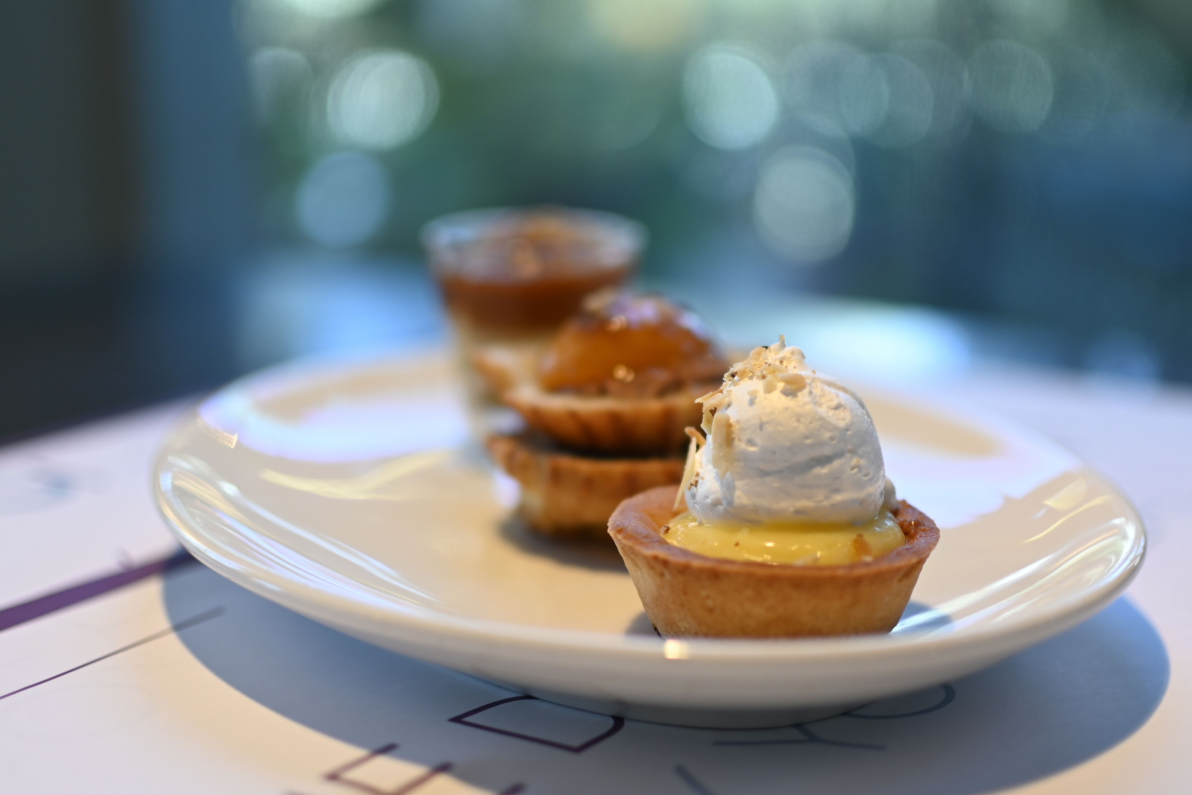 A plate with three small pastries, one topped with a dollop of cream.