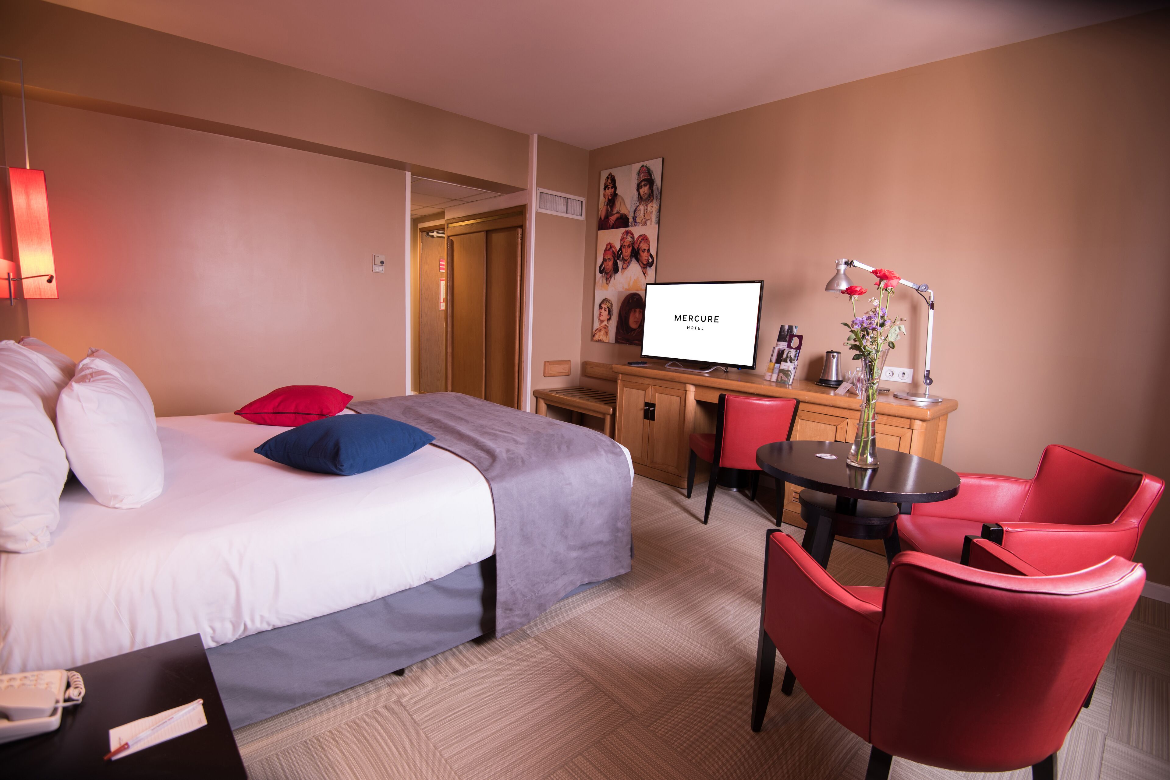 Una habitación de hotel con una cama, un escritorio, un televisor, una silla y una pequeña mesa con un florero.