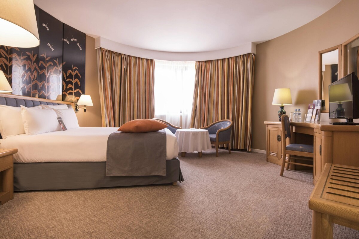 A hotel room with a bed, a desk, a chair, a television, and curtains.