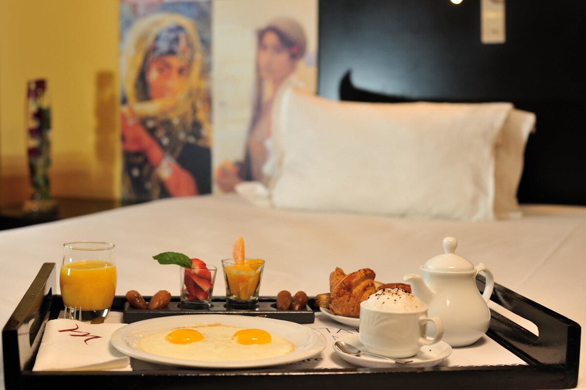 A breakfast tray with eggs, croissants, and juice on a hotel bed.